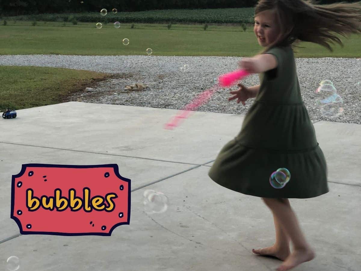 a little girl twirling with a bubble wand and text overlay that reads bubbles