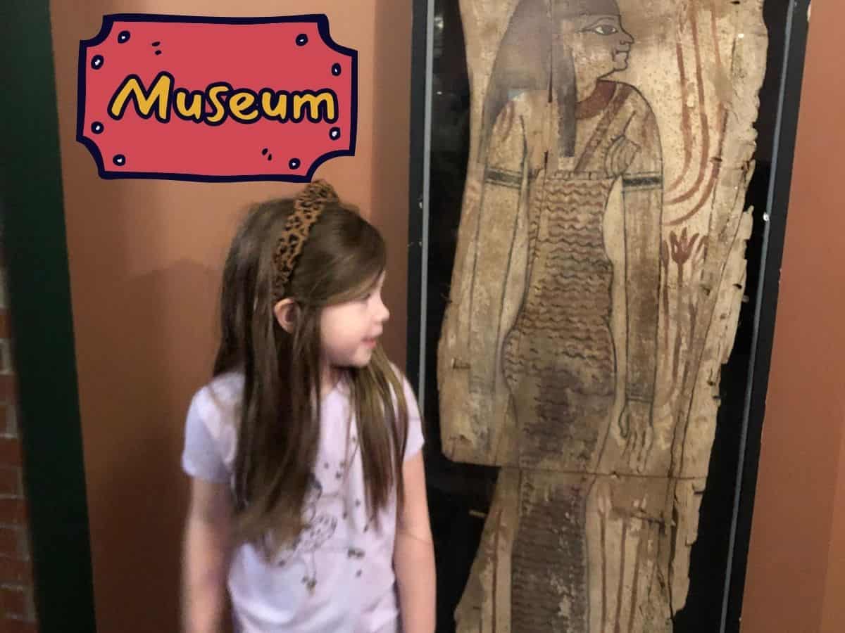 a little girl posing next to a egypt scroll at a museum with text overlay that reads Museum