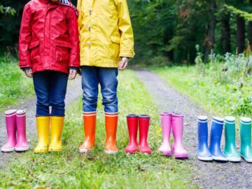 two kids wearing rain boots with five other pairs of boots next to them