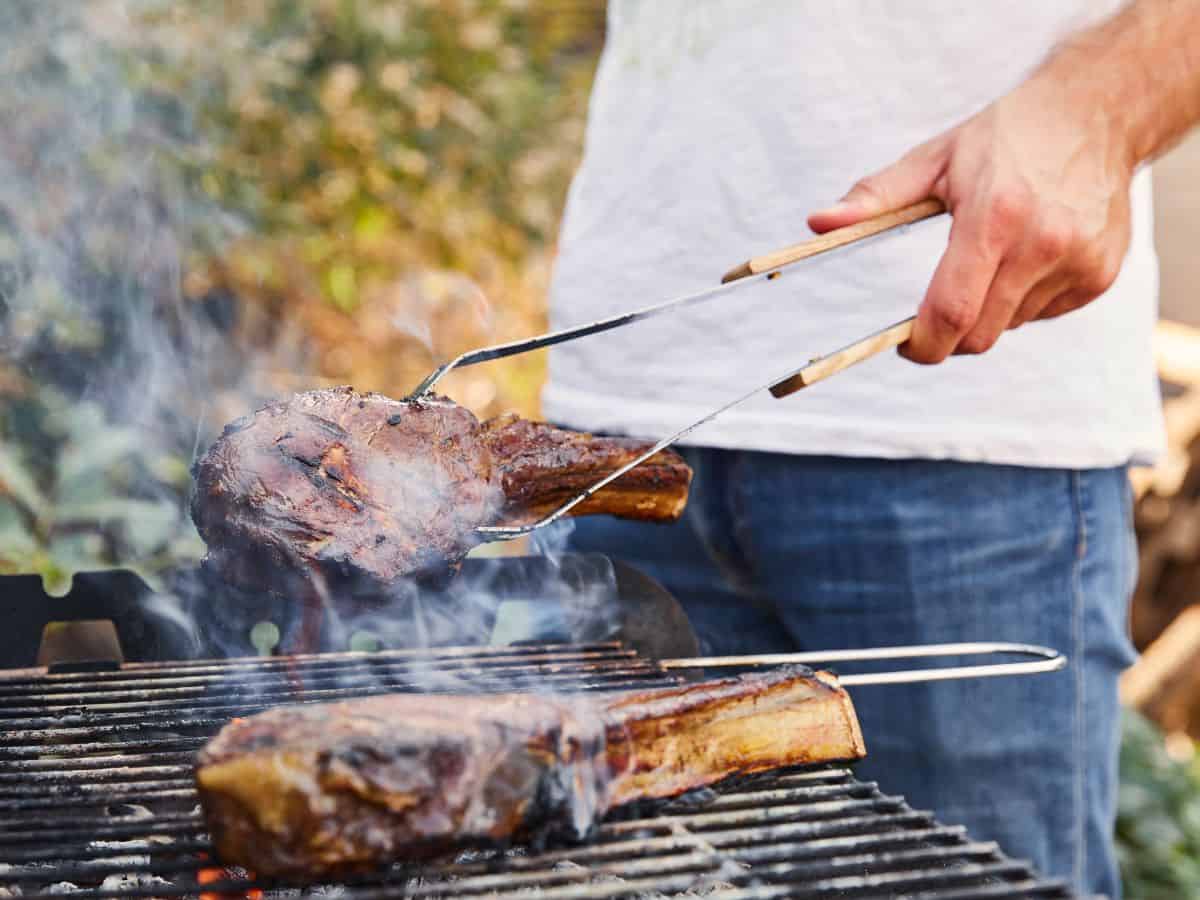 a man grilling two steaks on a barbecue grill