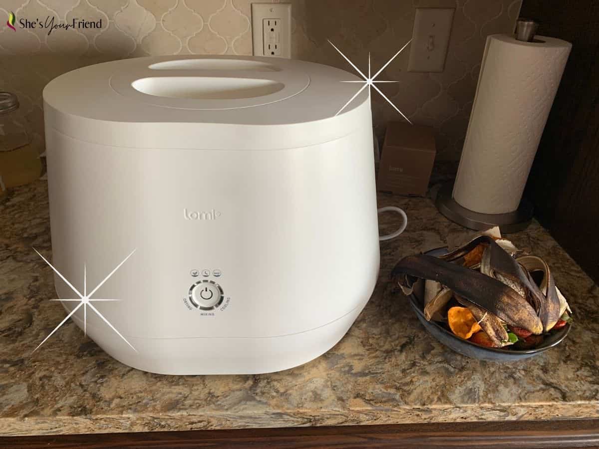 a Lomi smart composter on the counter top with a bowl of food scraps